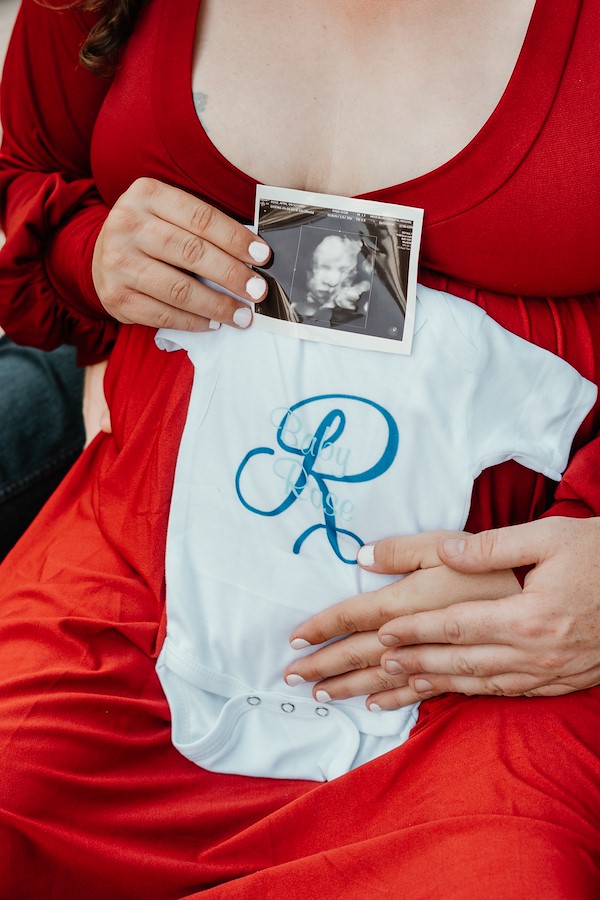 Mom and dad holding onesie and ultrasound in front of the barn at Rustic Ridge, Deridder, Louisiana