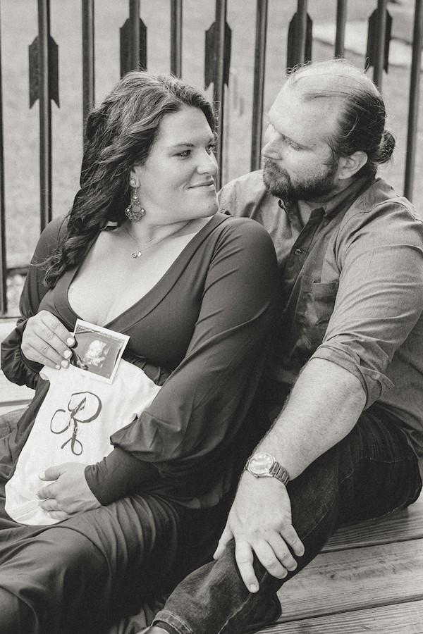 Mom and dad holding onesie and ultrasound in front of the barn at Rustic Ridge, Deridder, Louisiana